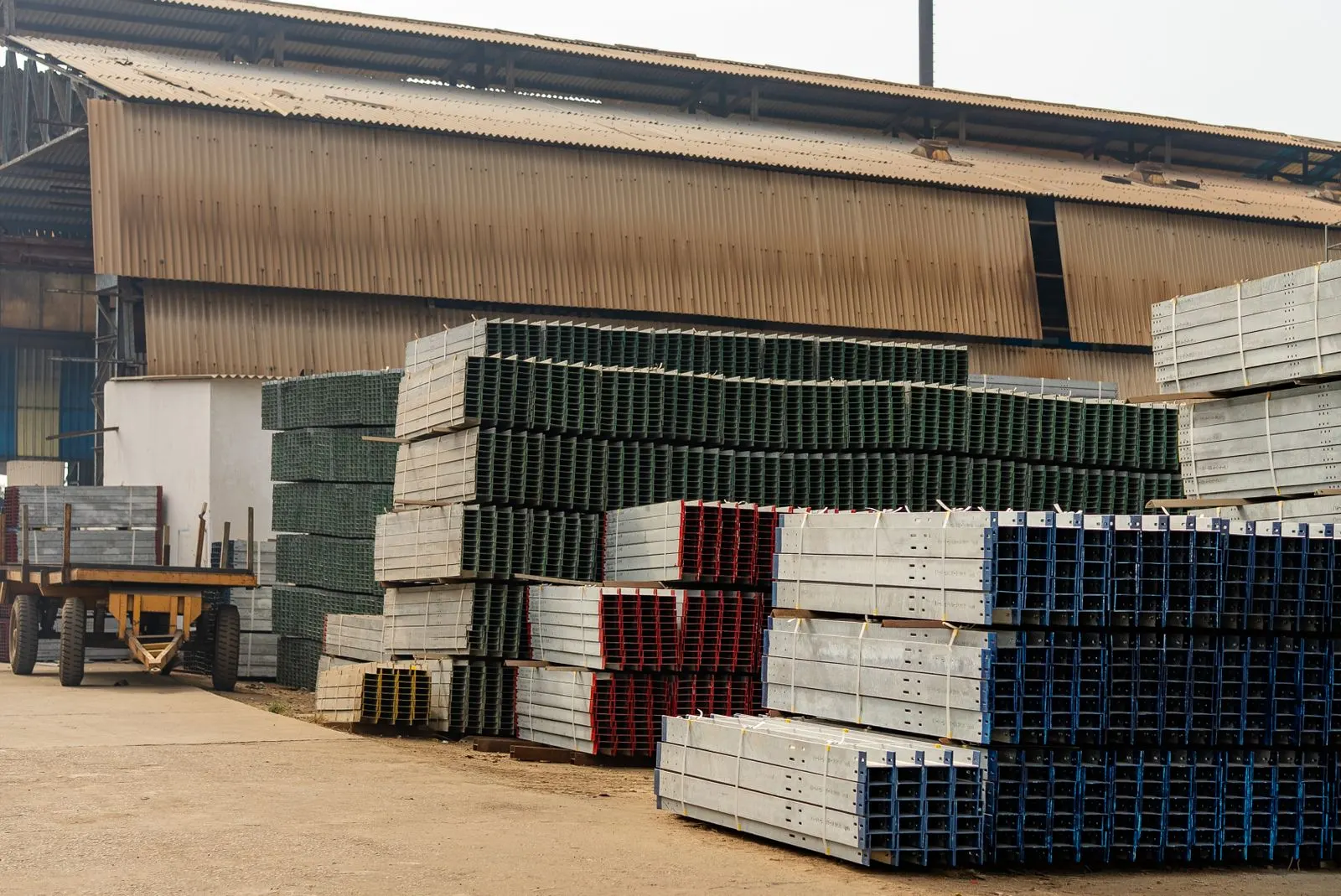 Stacks of galvanized steel profiles stored outside a warehouse