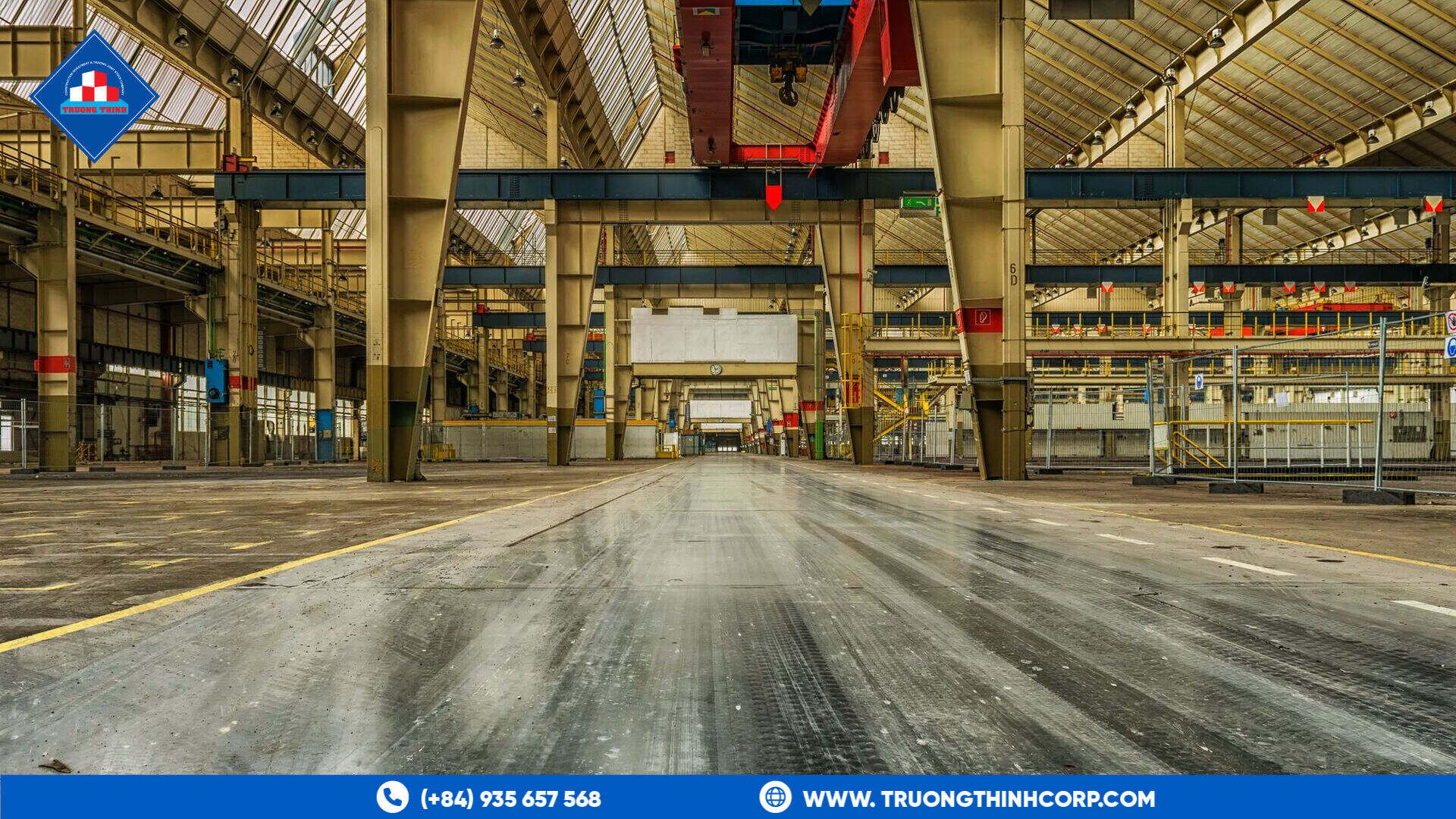 Wide interior view of an industrial steel-structure warehouse with overhead cranes