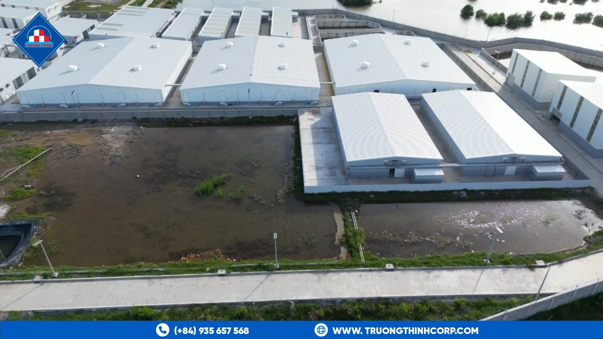 Aerial view of industrial buildings with metal roofs beside a water area at a Truong Thinh Corp project